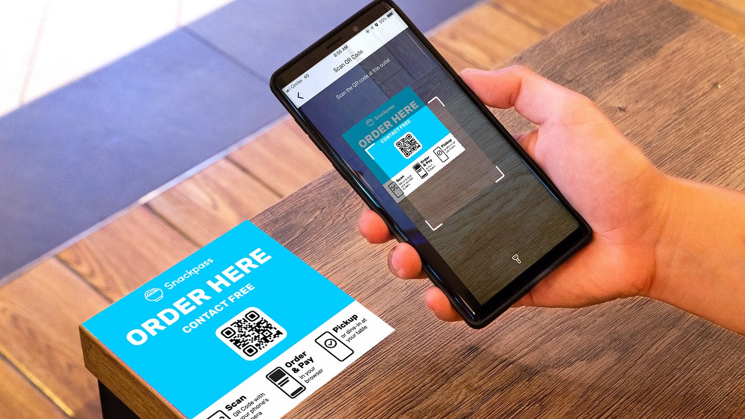 A phone scans a Snackpass āOrder Hereā QR code on a table to order and pay without contact.