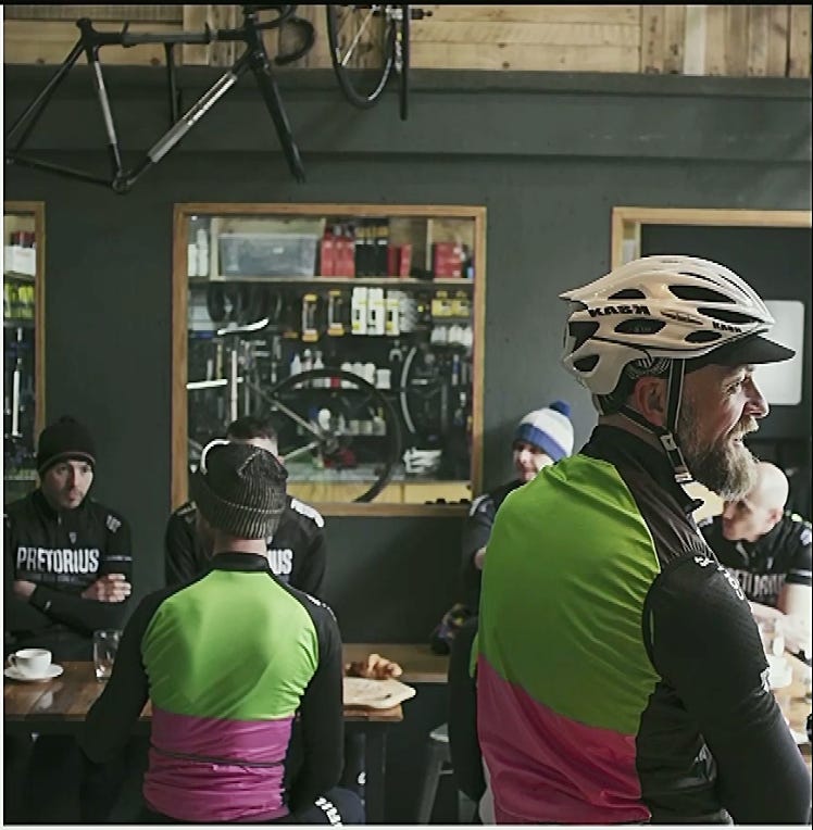 Cyclists in matching green and pink jerseys gather inside a cafe.